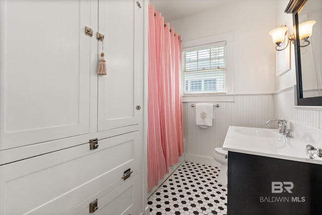 full bath with a shower with shower curtain, a wainscoted wall, toilet, and vanity