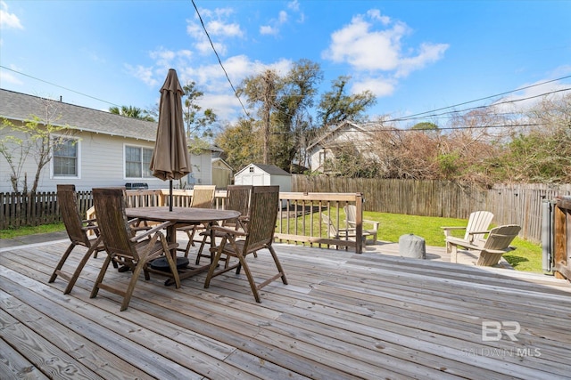 deck with a shed, a lawn, outdoor dining area, a fenced backyard, and an outbuilding