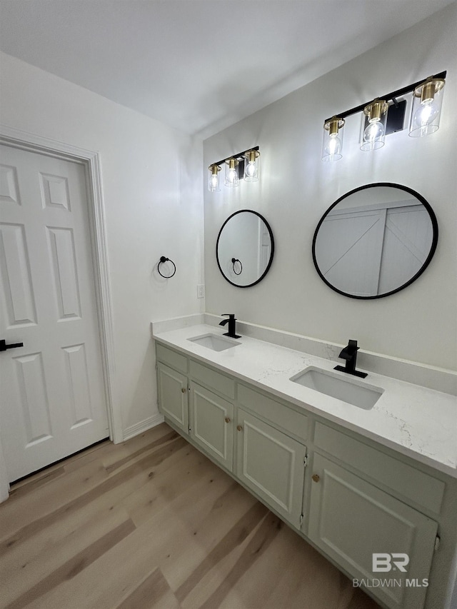 bathroom featuring baseboards, wood finished floors, a sink, and double vanity