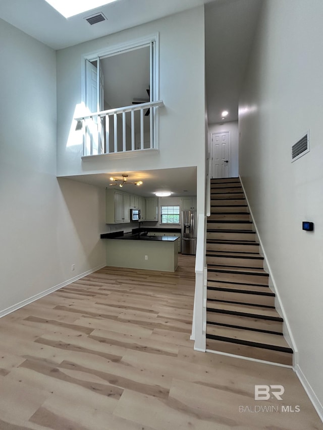 staircase featuring a high ceiling, baseboards, wood finished floors, and visible vents