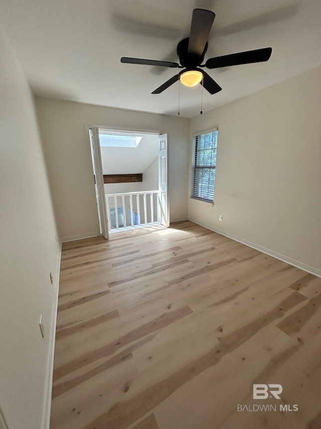 unfurnished room featuring wood finished floors, a skylight, baseboards, and a ceiling fan