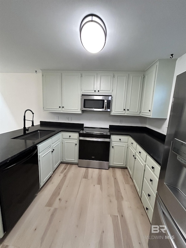 kitchen with light wood-type flooring, stainless steel appliances, a sink, and dark countertops