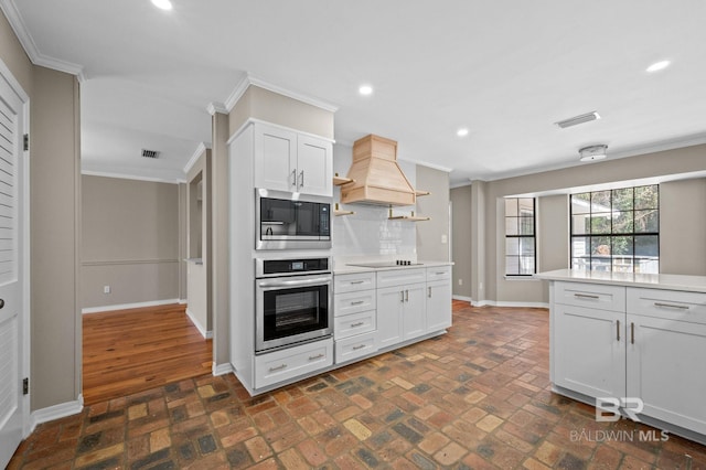 kitchen featuring stainless steel appliances, ornamental molding, brick floor, and custom exhaust hood