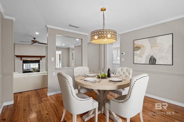 dining space featuring visible vents, baseboards, wood finished floors, crown molding, and a brick fireplace