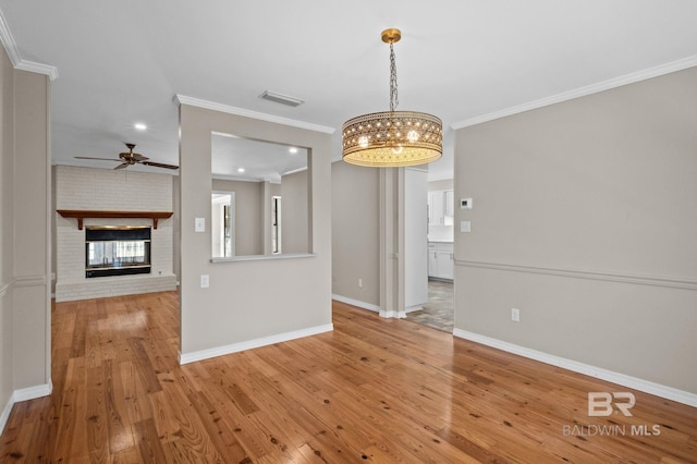 unfurnished dining area with a brick fireplace, baseboards, visible vents, ornamental molding, and light wood-style floors