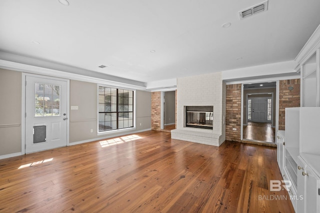 unfurnished living room with visible vents, hardwood / wood-style floors, a brick fireplace, brick wall, and baseboards