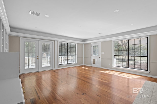 unfurnished living room with a healthy amount of sunlight, visible vents, hardwood / wood-style floors, and french doors