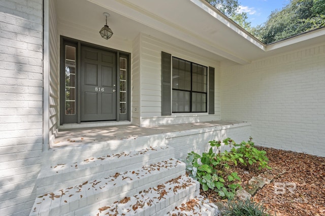 entrance to property with a porch and brick siding