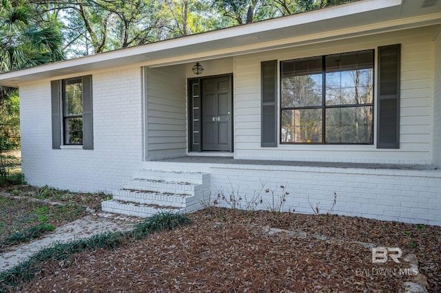 entrance to property featuring a porch and brick siding