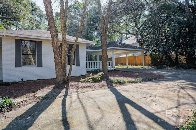 view of front of house with driveway, fence, a porch, a carport, and brick siding