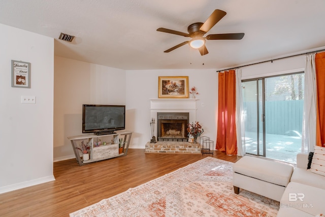 living room featuring ceiling fan, light hardwood / wood-style floors, and a brick fireplace