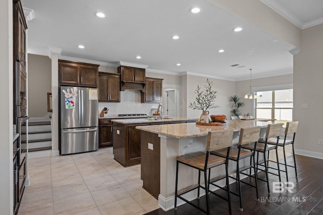 kitchen featuring pendant lighting, light stone countertops, an island with sink, a kitchen bar, and stainless steel appliances