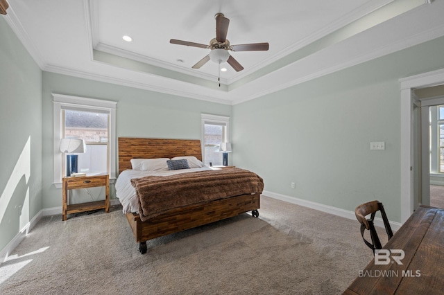 carpeted bedroom with a tray ceiling, multiple windows, ceiling fan, and ornamental molding