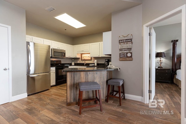 kitchen featuring stainless steel appliances, a peninsula, dark countertops, baseboards, and dark wood-style flooring