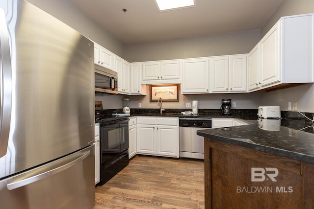 kitchen with stainless steel appliances, a sink, wood finished floors, and white cabinets