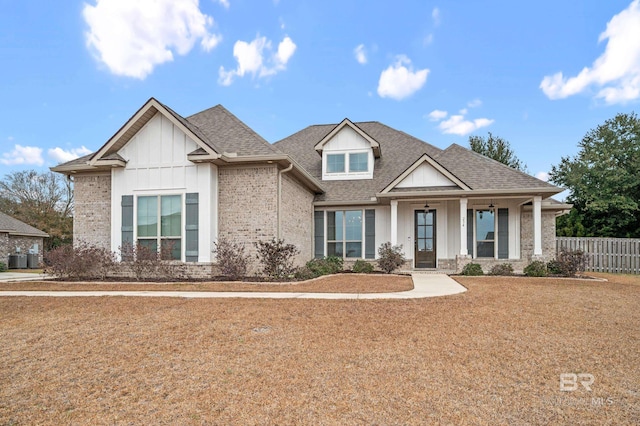 craftsman inspired home with a shingled roof, fence, a front lawn, board and batten siding, and brick siding