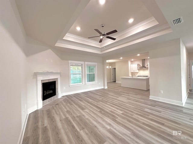 unfurnished living room featuring light wood-type flooring, a tray ceiling, a tile fireplace, and ceiling fan