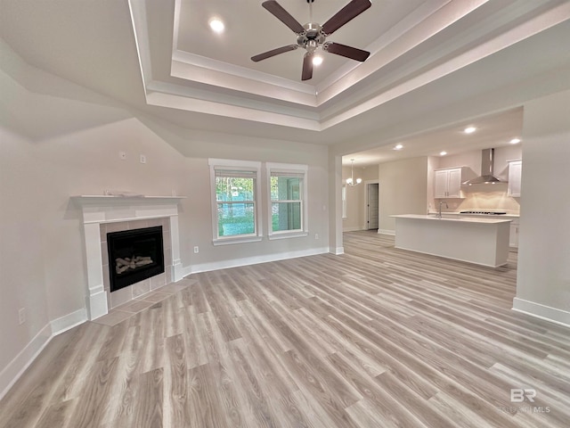 unfurnished living room featuring a tray ceiling, sink, light wood-type flooring, and a tiled fireplace