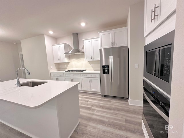 kitchen featuring appliances with stainless steel finishes, sink, white cabinetry, and wall chimney range hood