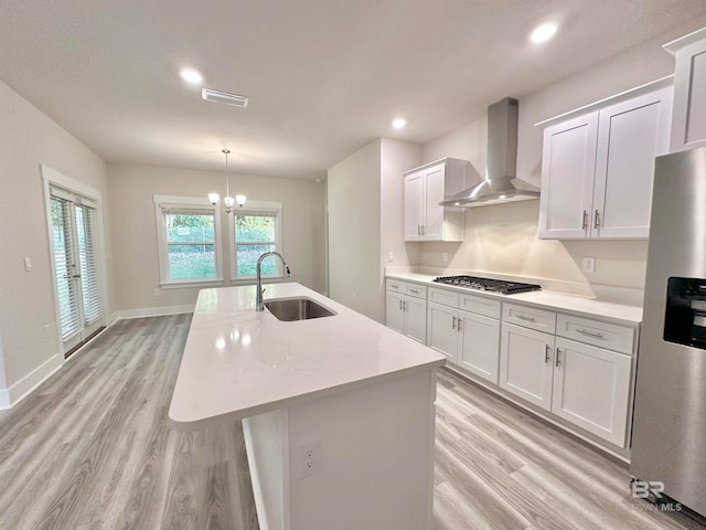 kitchen with a kitchen island with sink, sink, white cabinets, appliances with stainless steel finishes, and wall chimney range hood