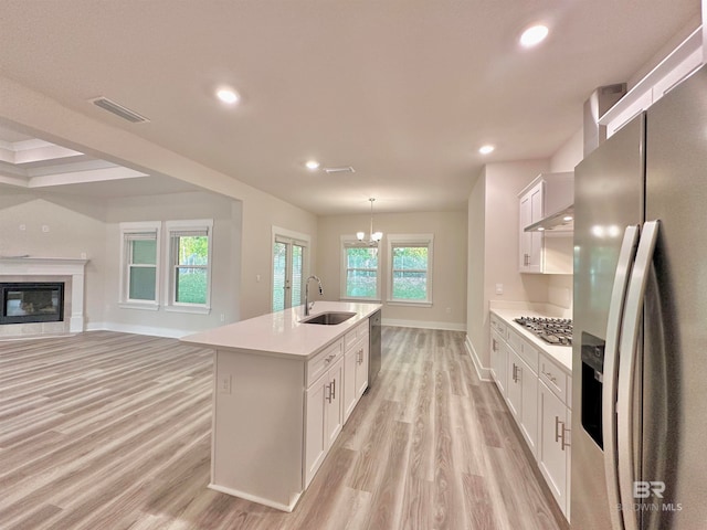 kitchen with stainless steel appliances, a center island with sink, sink, white cabinetry, and light wood-type flooring