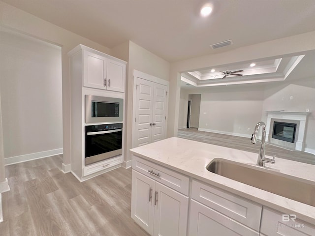 kitchen featuring sink, a tray ceiling, built in microwave, wall oven, and white cabinets