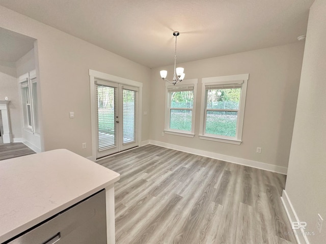 unfurnished dining area with a chandelier, light wood-type flooring, and french doors