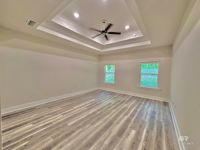 unfurnished room featuring light wood-type flooring, a tray ceiling, and ceiling fan