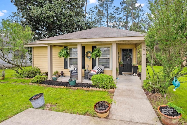 view of front of house featuring covered porch, a shingled roof, and a front yard