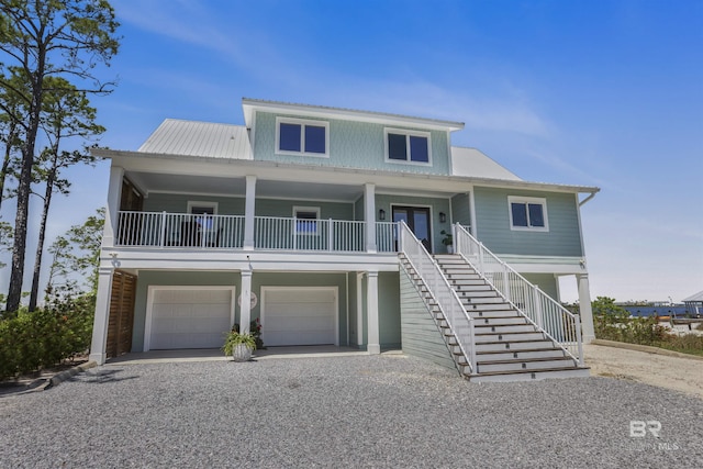 raised beach house featuring covered porch, metal roof, a garage, stairway, and gravel driveway