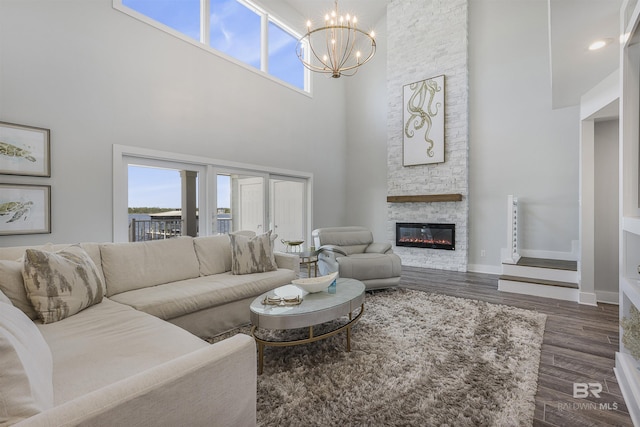living room with a chandelier, a towering ceiling, a stone fireplace, and a healthy amount of sunlight