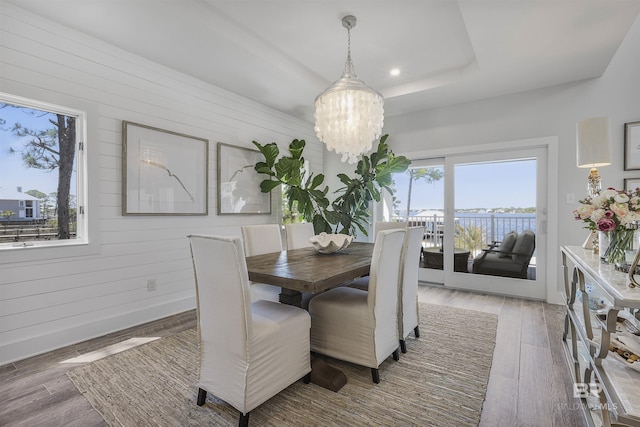 dining room featuring wood walls, baseboards, an inviting chandelier, and wood finished floors