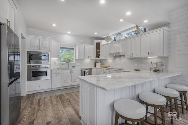 kitchen with wall chimney exhaust hood, a peninsula, white cabinetry, appliances with stainless steel finishes, and wood finished floors