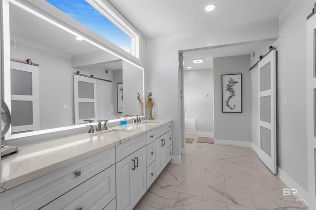 full bath with a sink, double vanity, marble finish floor, and recessed lighting