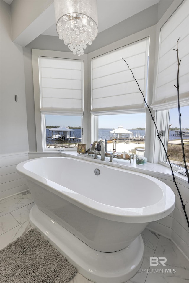 bathroom with a freestanding bath, a wealth of natural light, a notable chandelier, and marble finish floor