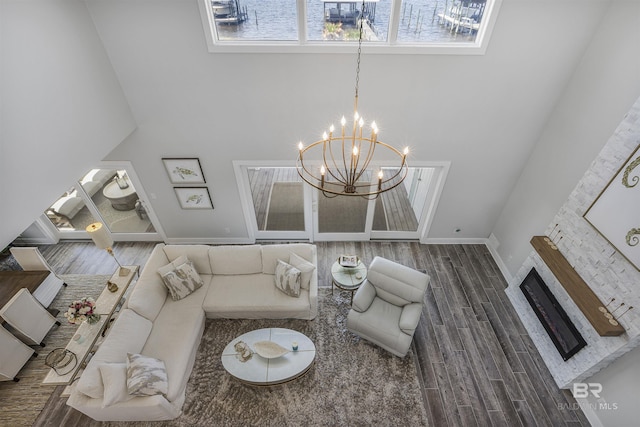 living room featuring an inviting chandelier, a glass covered fireplace, a high ceiling, wood finished floors, and baseboards