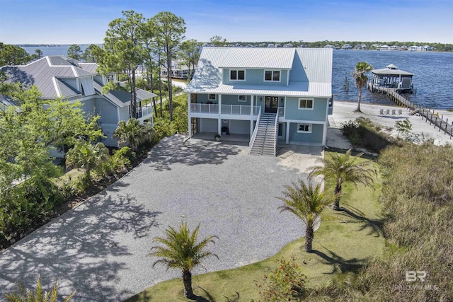 view of front of home with a garage, stairs, gravel driveway, a water view, and metal roof