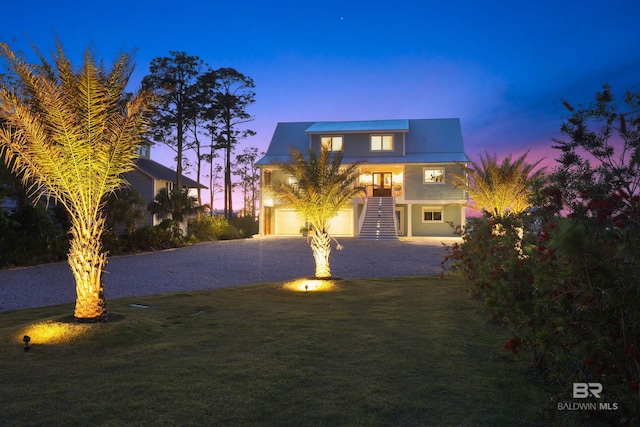 traditional home featuring stairway, an attached garage, gravel driveway, metal roof, and a lawn