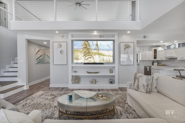 living area featuring a towering ceiling, baseboards, stairway, visible vents, and wood finished floors