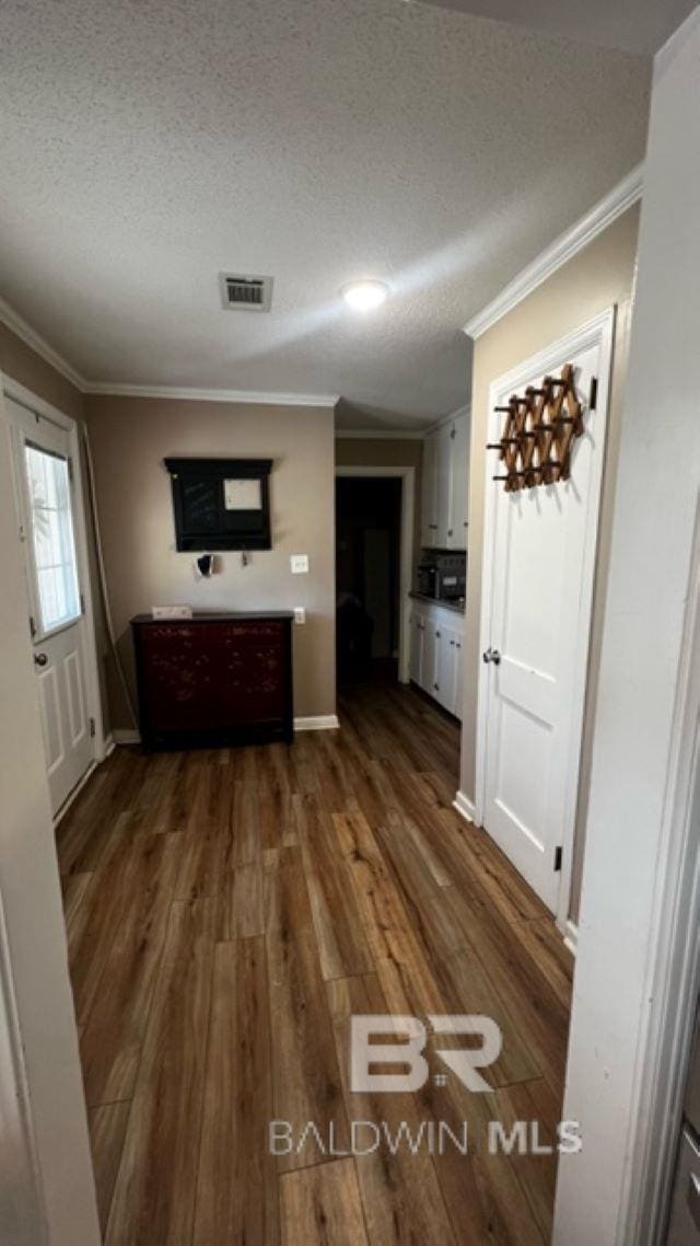 corridor featuring crown molding, dark wood-type flooring, and a textured ceiling