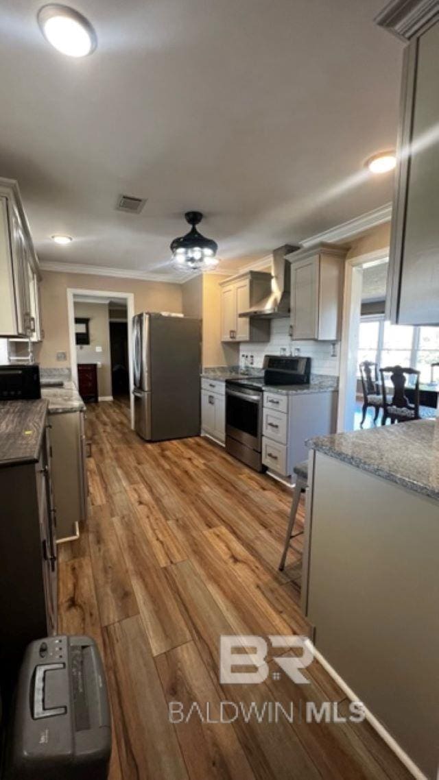 kitchen featuring light hardwood / wood-style floors, wall chimney range hood, stainless steel appliances, and ornamental molding