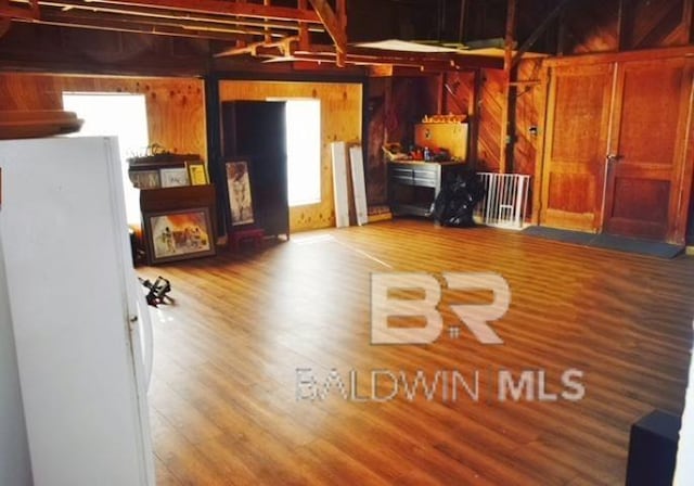 basement featuring wood walls, hardwood / wood-style floors, and white fridge