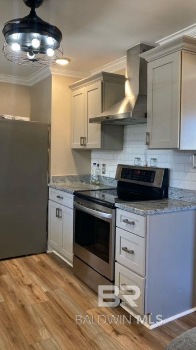 kitchen with appliances with stainless steel finishes, light hardwood / wood-style floors, crown molding, and wall chimney range hood