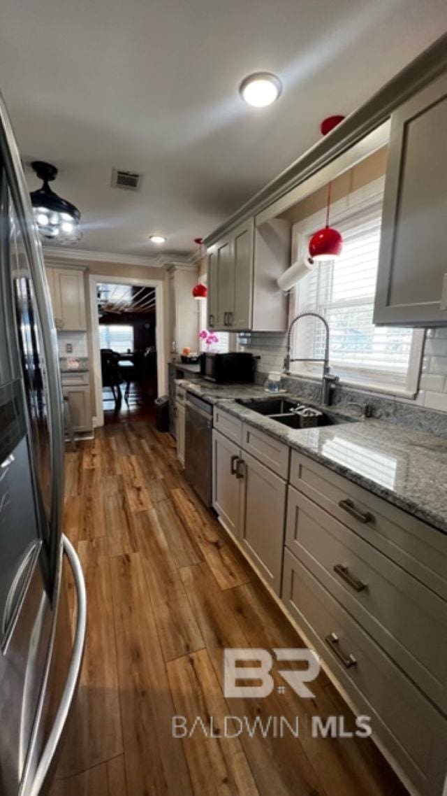 kitchen with dark wood-type flooring, hanging light fixtures, sink, light stone countertops, and appliances with stainless steel finishes