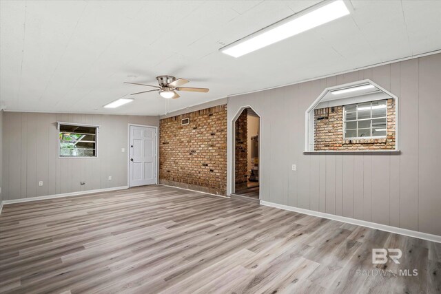 empty room with lofted ceiling, brick wall, ceiling fan, and light hardwood / wood-style floors