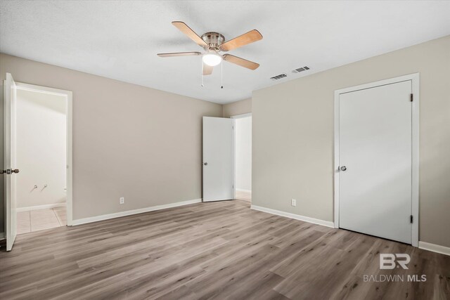 unfurnished bedroom with ceiling fan, ensuite bathroom, and light hardwood / wood-style floors