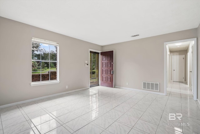 empty room with light tile patterned floors, visible vents, baseboards, and attic access