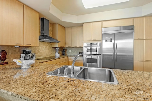 kitchen featuring kitchen peninsula, appliances with stainless steel finishes, wall chimney exhaust hood, sink, and light brown cabinets