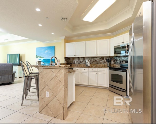 kitchen featuring visible vents, a tray ceiling, light tile patterned flooring, stainless steel appliances, and a kitchen bar