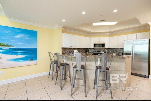 kitchen with a kitchen bar, crown molding, stainless steel appliances, and a raised ceiling